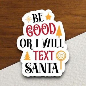 Op de afbeelding: Witte sticker met zwarte tekst die "Wees braaf, anders stuur ik een sms naar Sinterklaas" zegt. De sticker heeft ook een sneeuwvlok, een ster, een kerstboom en een lolly.