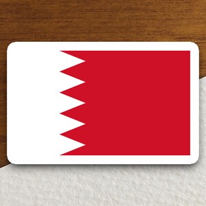 May include: A white sticker with the flag of Bahrain. The flag is red with a white serrated triangle on the hoist side.