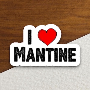 May include: A white sticker with the text "I ♥ MANTINE" in black, with a red heart replacing the word "love". The sticker is on a wooden surface.