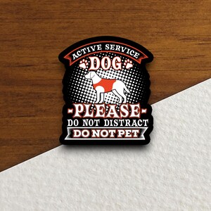 May include: Black and white sticker with a red and white dog wearing a vest that says "Active Service Dog". The sticker also says "Please - Do Not Distract - Do Not Pet".