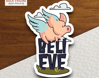 Può includere: Un adesivo fustellato raffigurante un maiale rosa chiaro con ali azzurre che vola sopra il testo viola scuro BELIEVE. Il design include nuvole bianche sullo sfondo e una piccola macchia di erba verde alla base delle lettere in grassetto.