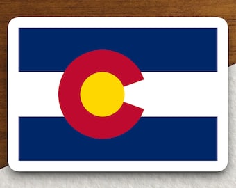 Pode incluir: Um adesivo com a bandeira do Colorado. A bandeira é azul com um grande 'C' branco no centro, rodeado por um círculo vermelho e um círculo amarelo no centro do círculo vermelho.