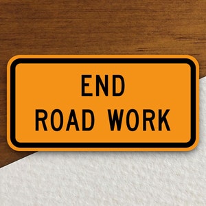May include: Orange and black road sign with the text "END ROAD WORK" on a wooden background.