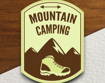 Könnte beinhalten: Ein brauner und gelber illustrierter Patch mit dem Text "Mountain Camping" und einem braunen Wanderschuh mit weißer Sohle auf einem braunen Bergrund.