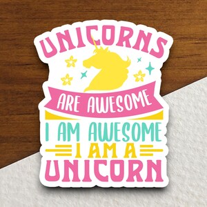 May include: A white sticker with the text "UNICORNS ARE AWESOME I AM AWESOME I AM A UNICORN" in pink, yellow, and teal. A yellow unicorn silhouette is in the center, with yellow stars and teal accents. The sticker is on a wooden surface.