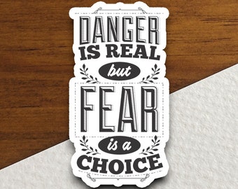 Puede incluir: Pegatina en blanco y negro con el texto "Danger is real but fear is a choice". El texto está en una fuente de estilo vintage con adornos decorativos.