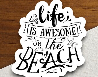 Könnte beinhalten: Schwarz-weißer Aufkleber mit dem Text "life is awesome on the beach" in einer handschriftlichen Schriftart. Der Aufkleber hat eine Muschel, einen Seestern und Wolken.