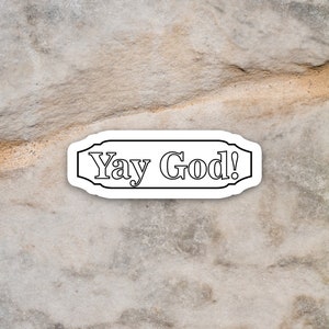 May include: A white sticker with black text that reads "Yay God!" on a textured, light brown background.