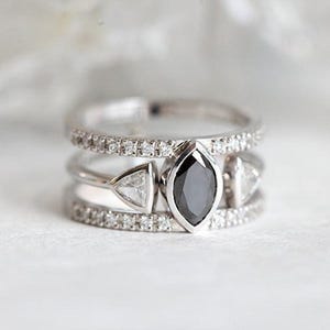 May include: A silver ring with three bands, each set with small diamonds. The center band features a larger, black marquise-shaped diamond.