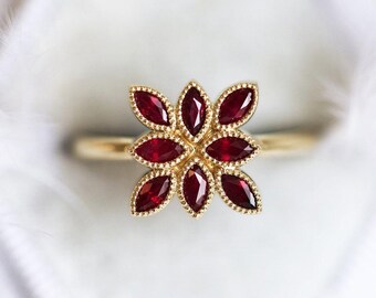 Op de afbeelding: Een gouden ring met een rood robijn bloemenontwerp. De ring heeft acht robijnstenen die in de vorm van een bloem zijn gezet.