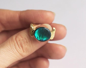 Op de afbeelding: Een gouden ring met een ronde, groene edelsteen in het midden. De ring heeft een getextureerde band.