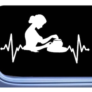 May include: A white silhouette of a person working on a pottery wheel with a heartbeat graphic on either side. The image is on a black background.