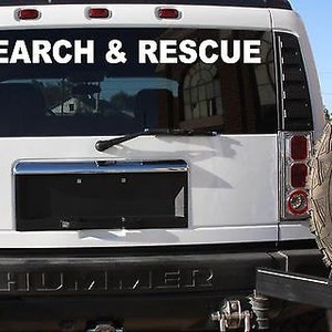 Op de afbeelding: Witte Hummer met een "SEARCH & RESCUE" sticker op de achterruit. Het voertuig heeft een zwarte kentekenplaatbedekking en een reservewiel achterop.