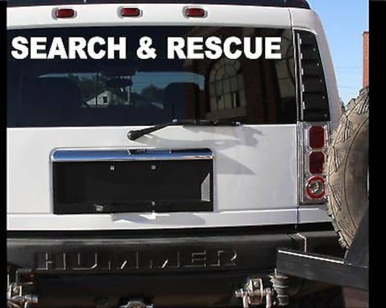 Op de afbeelding: Witte Hummer met een "SEARCH & RESCUE" sticker op de achterruit. Het voertuig heeft een zwarte kentekenplaatbedekking en een reservewiel achterop.