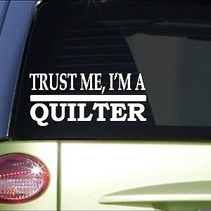 May include: White vinyl decal with the text "Trust me, I'm a quilter" on a black car window.