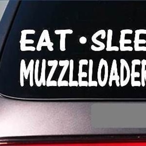 May include: White vinyl decal with the text "EAT - SLEEP MUZZLELOADERS" on a black background. The decal is applied to the rear window of a car.