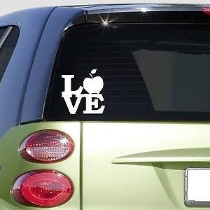May include: White vinyl decal with the word "LOVE" with an apple replacing the "O". The decal is on the back window of a green car.