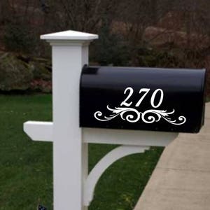 Op de afbeelding: Witte sticker met huisnummer voor de brievenbus met een decoratief scroll-ontwerp. Het nummer 270 staat op de sticker.