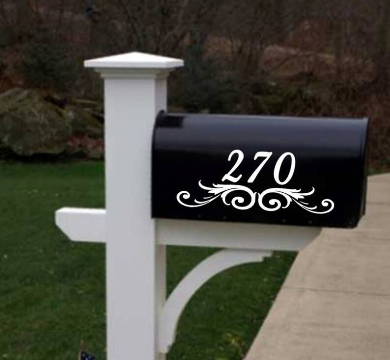 Op de afbeelding: Witte sticker met huisnummer voor de brievenbus met een decoratief scroll-ontwerp. Het nummer 270 staat op de sticker.