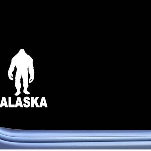 May include: A white vinyl sticker with a silhouette of Bigfoot and the word "ALASKA" underneath.