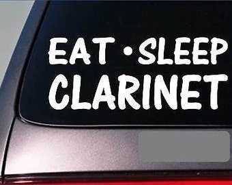 May include: A white vinyl decal with the text "Eat - Sleep Clarinet" on a black background. The decal is attached to the back window of a car.