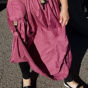 Peut inclure: Une femme portant une longue jupe bordeaux avec une grande poche sur le devant. La jupe a une taille à cordon et est faite d'un tissu léger et résistant à l'eau.