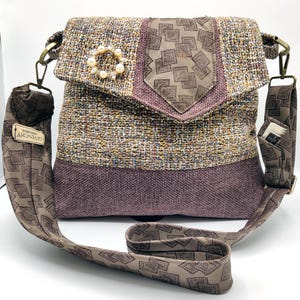 May include: A tweed crossbody bag with a flap closure, featuring a pearl brooch and a patterned strap. The bag combines brown, purple, and tan hues. The strap and flap have a geometric design. The bag has a Givenchy tag.