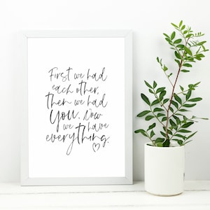 Puede incluir: Una impresión enmarcada en blanco con caligrafía negra que dice "First we had each other, then we had you. Now we have everything." con un pequeño símbolo de corazón al final.