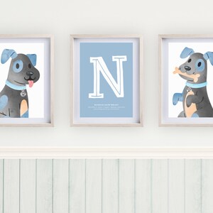 Puede incluir: Tres impresiones enmarcadas con una ilustración de acuarela azul y gris de un perro. La impresión central presenta la letra "N" en un contorno blanco sobre un fondo azul claro. El texto "Nicholas Landon Wright" está debajo de la letra.