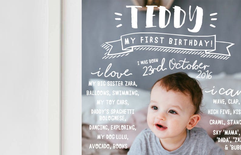 May include: A chalkboard with a photo of a baby boy celebrating his first birthday. The chalkboard says "Teddy, My First Birthday! I was born 23rd October 2016. I love my big sister Zara, balloons, swimming, my toy cars, Daddy's spaghetti bolognese, dancing, exploring, my dog Lulu, avocado, books. I can wave, clap, high five, kiss, crawl, stand, say 'Mama', 'Dada', 'Zara' & 'Bubbles'."