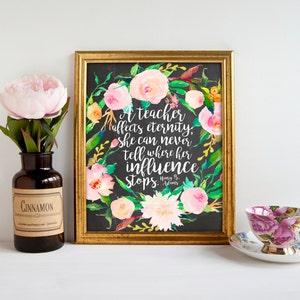 Puede incluir: Una impresión enmarcada en dorado con fondo negro y una corona floral de acuarela. La cita dentro de la corona dice: "Un maestro afecta la eternidad. Ella nunca puede decir dónde termina su influencia. - Henry B. Adams".