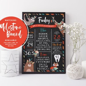 May include: A black chalkboard style milestone poster with a colorful tribal design. The poster features a sloth, a deer, a bear, and a fox. The text on the poster reads "Finley, My First Birthday!" and includes details about the child's birthdate, weight, height, and favorite foods.
