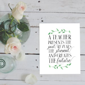 May include: A white card with green leafy vines around the edges. The text on the card reads "A teacher presents the past, reveals the present, and creates the future!"