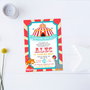 May include: A red and white striped circus tent with a blue banner that says "Come One, Come All!"  The text below the banner says "Step Right Up and Join in the Fun! The Magnificent Alec is Turning One!"  The invitation also includes the date and time of the event, as well as the address.  There are illustrations of a tiger, a seal, and a ball.