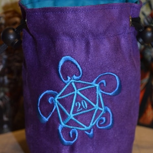 May include: Purple velvet dice bag with a blue embroidered design of a 20-sided die inside a turtle shell.