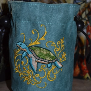 May include: Teal suede dice bag with a gold embroidered sea turtle and floral design.