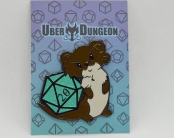 May include: A pin featuring a cartoon otter holding a teal D20 die with the number 20. The otter is brown and white, with the text "UBER DUNGEON" at the top. The background is a gradient of blue and purple with geometric shapes.