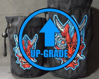 May include: Two black dice bags with red and blue embroidered demon faces. The larger bag is labeled "UP-GRADE" in a blue circle with an arrow pointing up.
