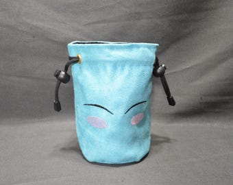 May include: A light blue drawstring pouch with a cartoon face embroidered on the front. The face has black curved lines for eyes and pink blush marks. The pouch has a black drawstring closure and black accents.