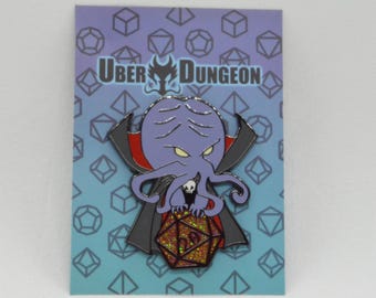 May include: A purple octopus-like creature with a vampire cape and a D20 die, on a card with the text "Uber Dungeon". The pin has a skull and is set against a blue background with geometric shapes.