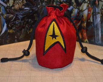 May include: Red drawstring bag with a gold and black embroidered emblem. The bag has a black drawstring closure and is likely used for storing small items. The background features a fantasy-themed illustration.