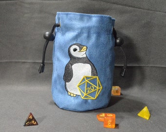 May include: Blue velvet dice bag with an embroidered penguin holding a 20-sided die. The bag has a drawstring closure with black beads.