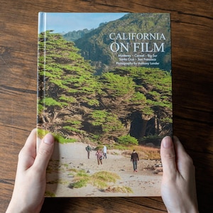 May include: A hardcover book titled California on Film, featuring photography by Anthony Londer. The cover displays a landscape image of a sandy beach with green trees and three people walking, with text listing Monterey, Carmel, Big Sur, Santa Cruz, and San Francisco.