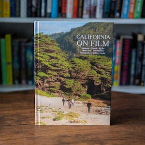 May include: A hardcover book titled California on Film with photography by Anthony Londer. The cover features a landscape image of a sandy beach with green trees, hills, and four people walking. The text includes Monterey, Carmel, Big Sur, Santa Cruz, and San Francisco.
