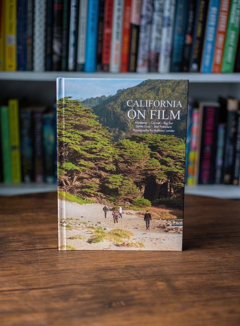 May include: A hardcover book titled California on Film with photography by Anthony Londer. The cover features a landscape image of a sandy beach with green trees, hills, and four people walking. The text includes Monterey, Carmel, Big Sur, Santa Cruz, and San Francisco.