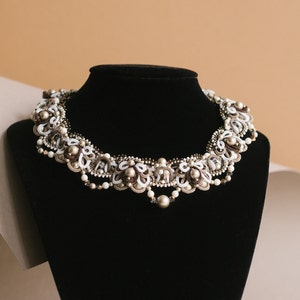 Peut inclure: Un collier de perles blanches et brunes avec un motif floral. Le collier est sur un support en velours noir.