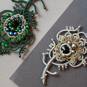 Könnte beinhalten: Zwei komplizierte gehäkelte Broschen mit Perlenbesatz. Eine ist grün mit blauen und grünen Perlen, die andere ist silber mit schwarzen und weißen Perlen.