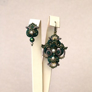 May include: A pair of green and silver earrings with intricate designs and pearl accents. The earrings are displayed on white stands.
