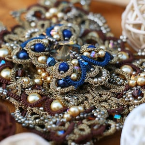 Könnte beinhalten: Eine Nahaufnahme einer braunen, goldenen und blauen Perlenkette mit aufwendigen Häkeldetails. Die Kette besteht aus verschiedenen Perlen, darunter Perlen, Kristalle und Glasperlen.