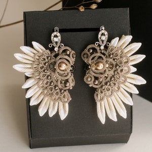 May include: A pair of delicate earrings with a lace-like design, featuring a white and brown colour scheme. The earrings are adorned with small pearls and rhinestones.